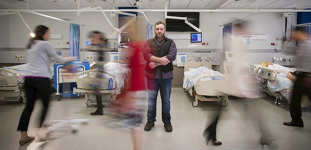 picture of a man stood in a hospital ward with lots of nurses and doctors rushing around him. Long exposure image.